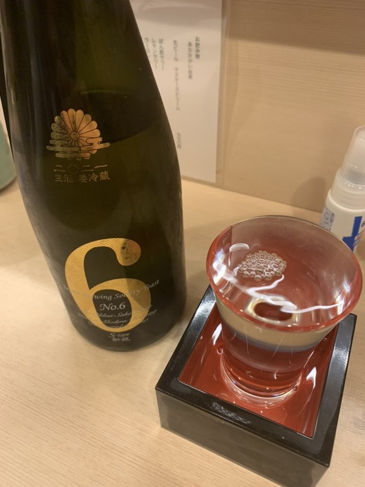 An Aramasa No. 6 S-type bottle, dark green with a gold 6 and chrysanthemum crest, beside a red glass cup