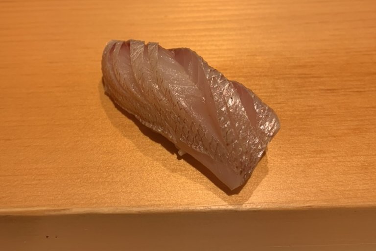 A pale kasugo nigiri on the wooden counter