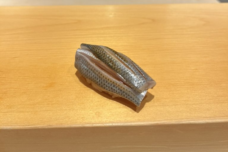 A kohada nigiri with finely dotted silver skin, made from two small fillets, on the wooden counter