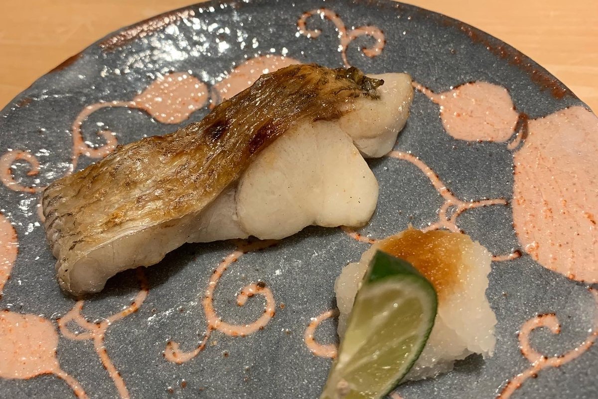 Roasted nodoguro on a grey plate with a wedge of sudachi and grated daikon