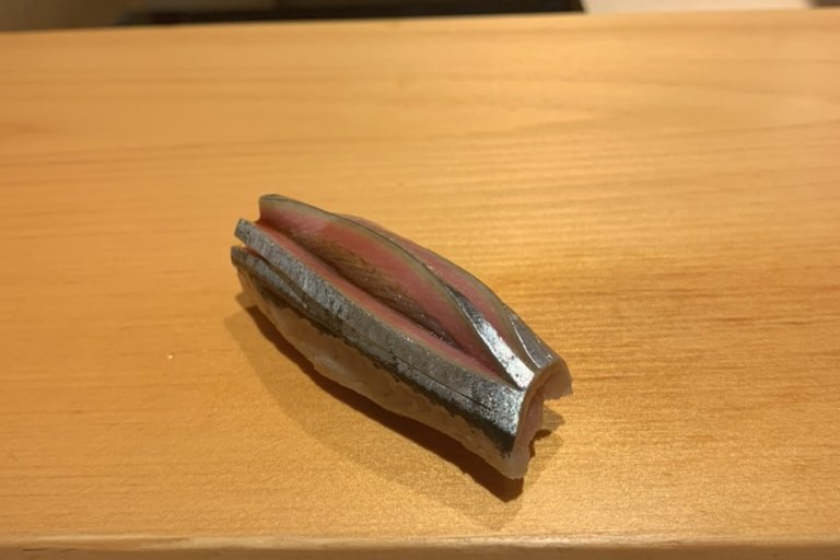 A silver-skinned sanma nigiri on the wooden counter