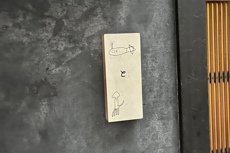 Hide's discreet entrance — a small stone sign with a hand-drawn squid on a dark plaster wall beside a wooden lattice door
