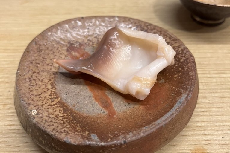 A lightly grilled hokkigai surf clam on a rustic ceramic plate