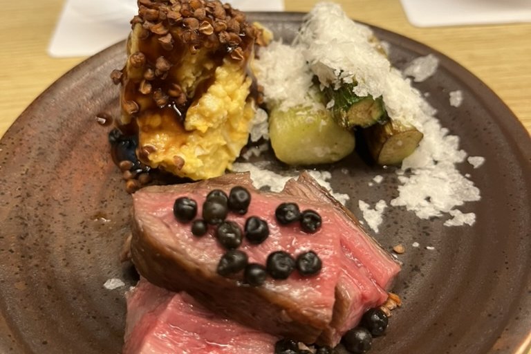 Slices of rare grilled wagyu with black peppercorns, a crusted side, vegetables and salt on a brown plate