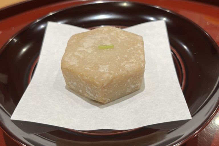 A fried hexagonal piece of ebi-imo Kyoto taro on white paper in a dark lacquer bowl