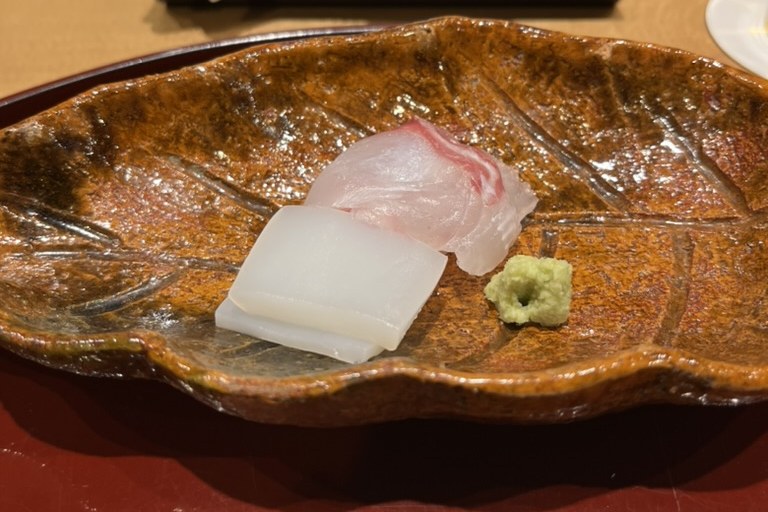 Squid and sea bream sashimi with a mound of grated wasabi on a leaf-shaped brown plate