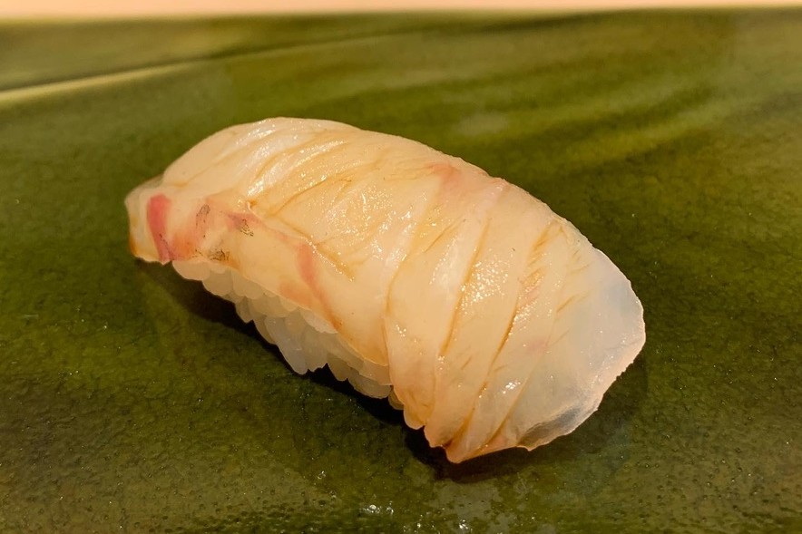 A madai (red sea bream) nigiri, pale translucent white fish with faint pink skin lines, on a green oribe plate at Sushi Mizukami