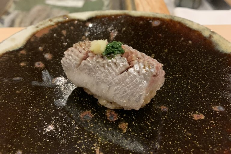 An aged iwashi (sardine) nigiri topped with grated ginger and scallion on a dark gold-flecked plate
