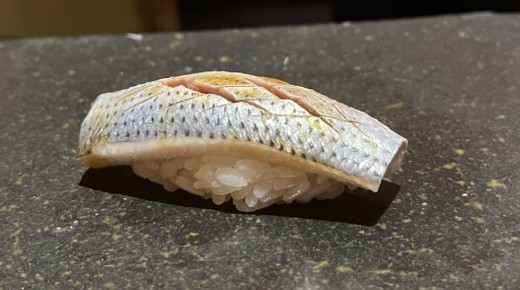A piece of kohada nigiri with scored silver skin on a dark stone plate