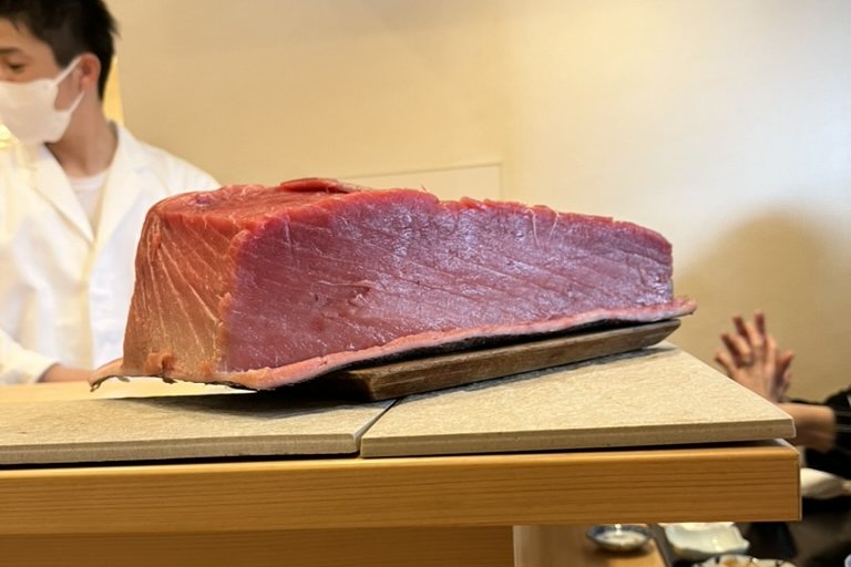 A large block of bluefin tuna loin resting on the counter, the chef standing behind