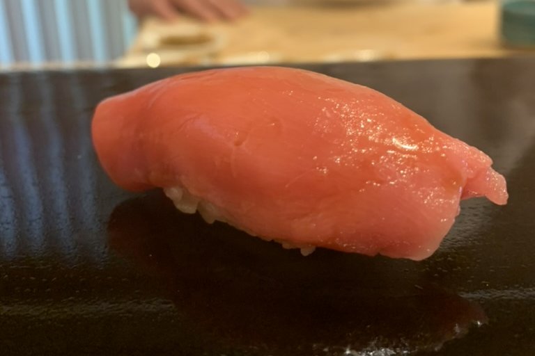 A pale, soft chūtoro nigiri on a black lacquer plate