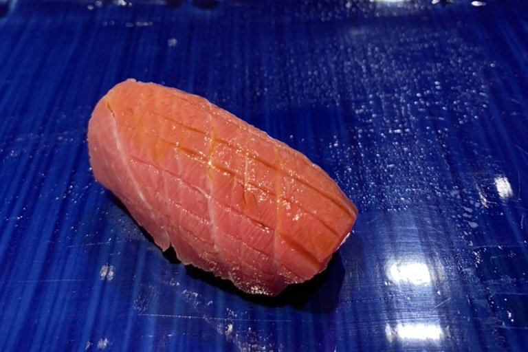 An ōtoro nigiri on a cobalt-blue plate, pale pink and heavily marbled with fat