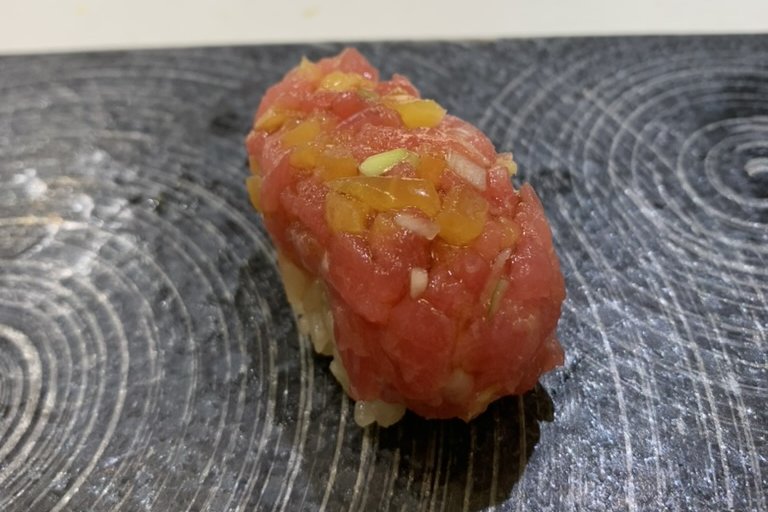 A nigiri topped with chopped tuna mixed with diced yellow takuan pickle