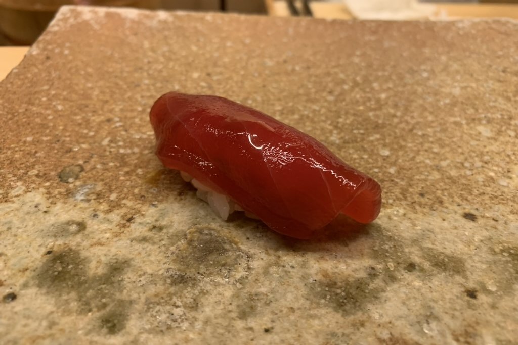 A deep-red akami nigiri, glossy from a soy marinade, on a stone plate