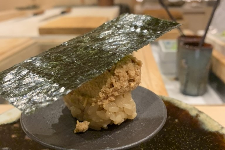 Warm rice topped with pale monkfish-liver paste under a draped sheet of nori, on a small pedestal