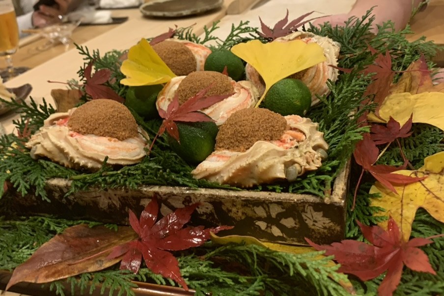 A wooden tray of crab shells packed with picked meat and miso, dressed with red and yellow autumn leaves, cedar and sudachi
