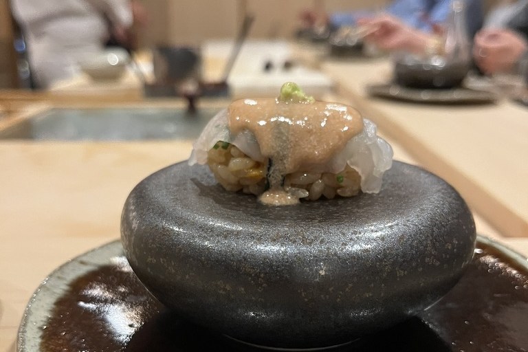 A kawahagi nigiri dressed with its own pale liver, set on a round black stone