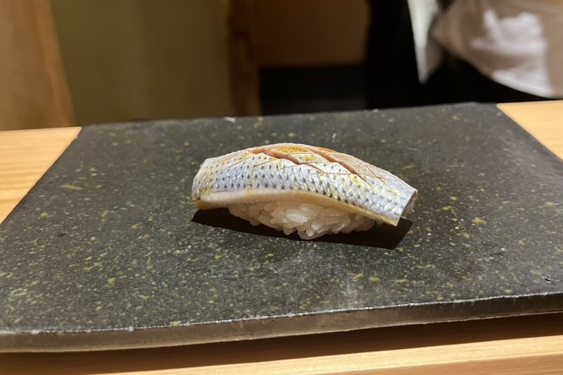 A kohada nigiri with finely scored silver skin on a dark stone plate