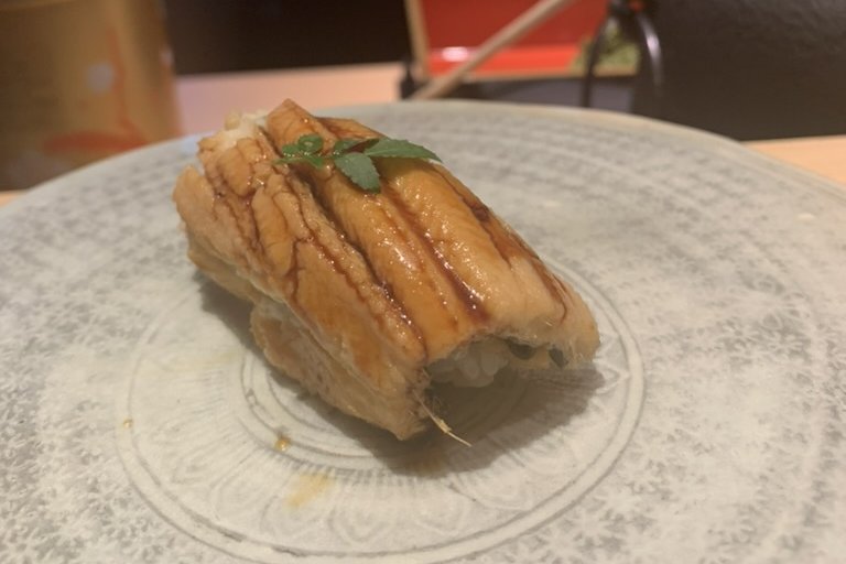 An anago sea eel nigiri, glazed, topped with a sprig of kinome