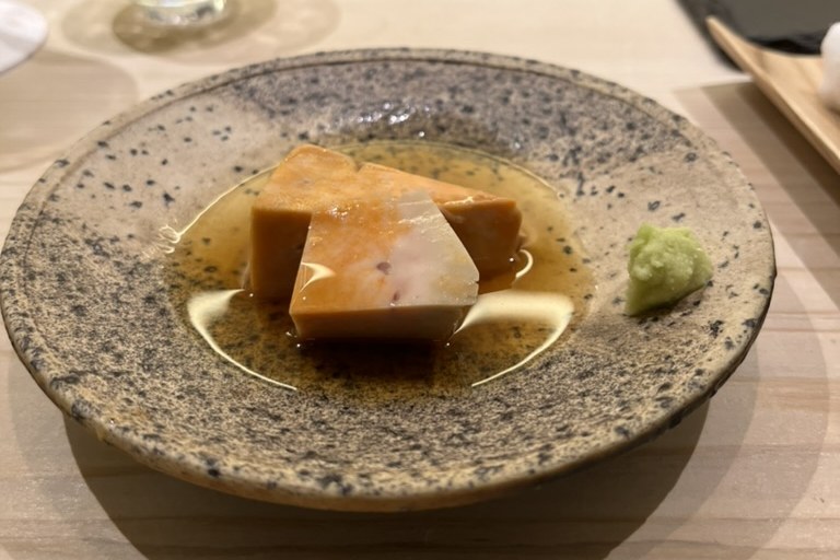 A block of monkfish liver in a light ponzu with a dab of wasabi on a speckled plate