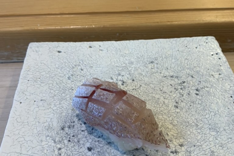 A young sea bream nigiri with finely scored skin on a white speckled plate