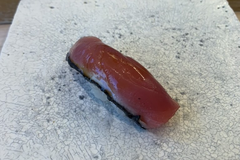 A deep-red bonito nigiri with a dark seam of skin on a white plate