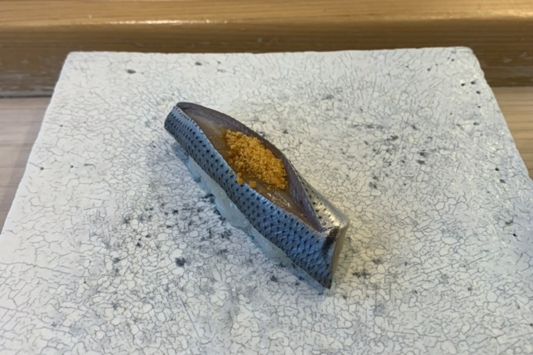 A gizzard shad nigiri with blue-silver scored skin, topped with a little grated ginger