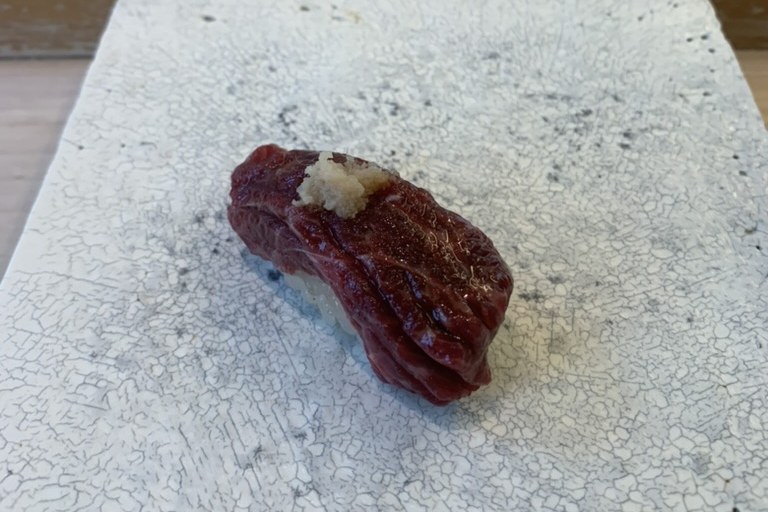 A dark red whale-meat nigiri topped with a little grated ginger on a white plate