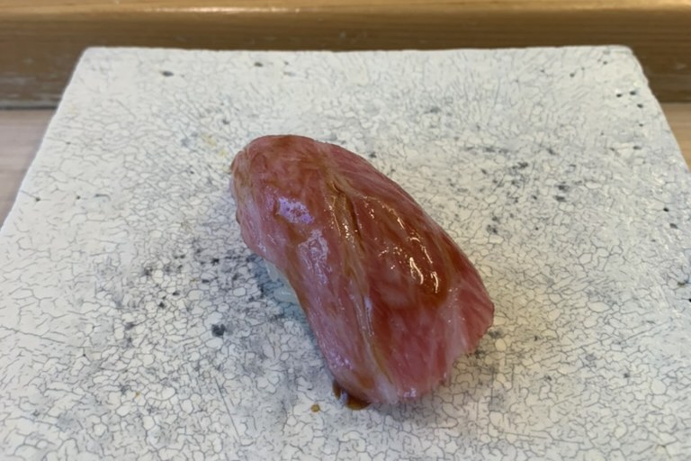 A heavily marbled otoro nigiri, pale pink with fat, on a white speckled plate
