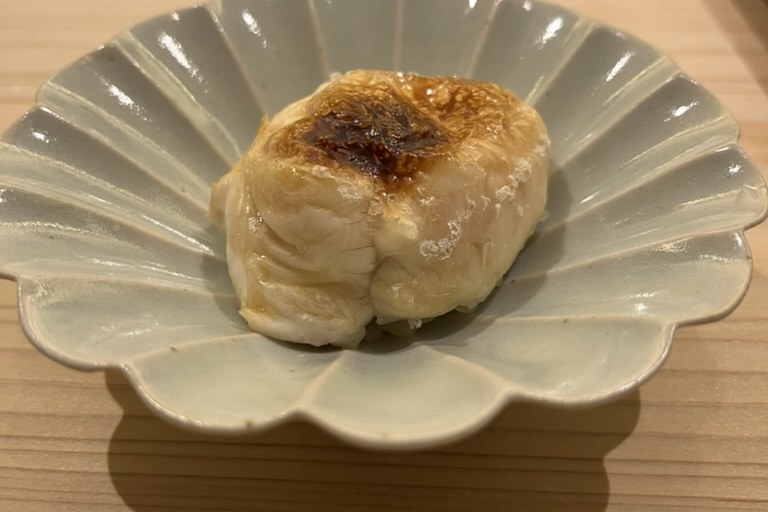 A lightly torched piece of pufferfish milt, browned on top, on a pale chrysanthemum dish