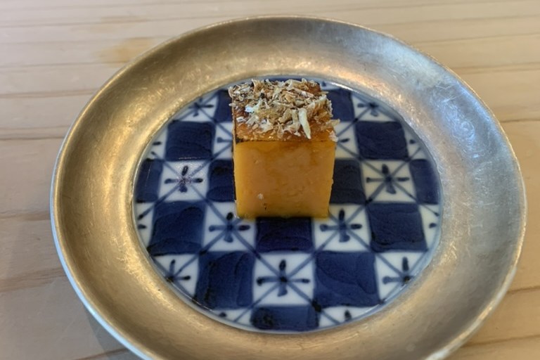 A dense orange cube of tamago topped with a savoury crumb on a blue-and-white patterned plate