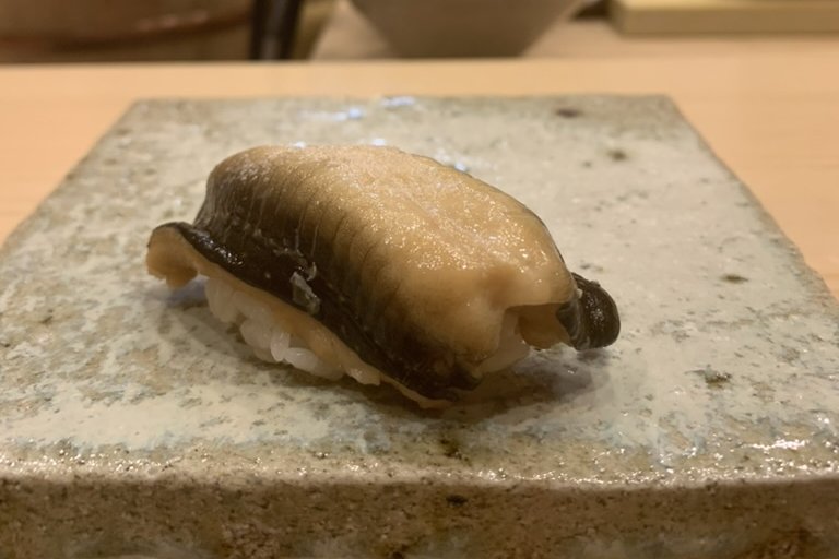 An anago nigiri on a stone plate, the sea eel simmered soft and brushed with a sweet glaze