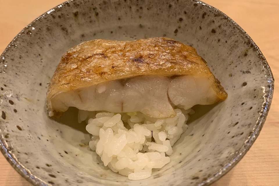 A large seared piece of nodoguro (rosy seabass) on rice in a speckled blue ceramic bowl