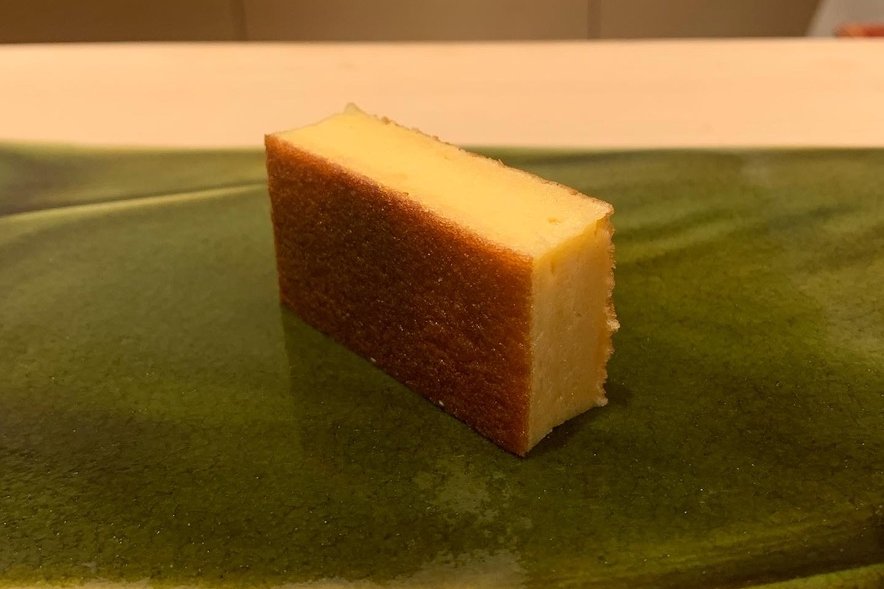 A block of castella-style tamago on a green plate, browned at the edges with a pale sweet interior