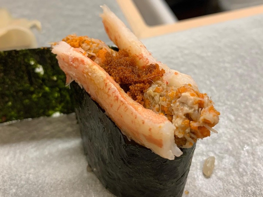 A crab gunkan wrapped in nori, topped with a whole crab leg, shredded crab meat, and orange roe