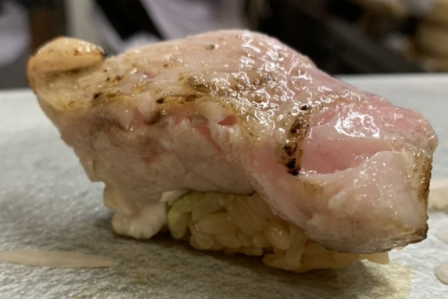 A seared nodoguro nigiri, fatty white fish with light grill marks, on a pale stone plate