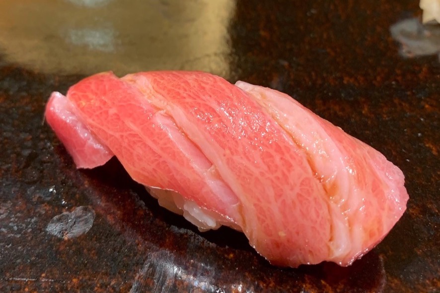A heavily marbled otoro (fatty bluefin tuna) nigiri on a dark glazed plate