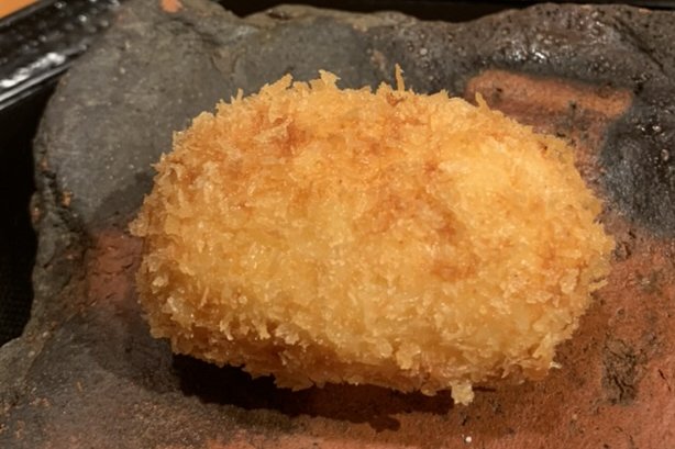 A golden-fried cream croquette on a dark stone plate