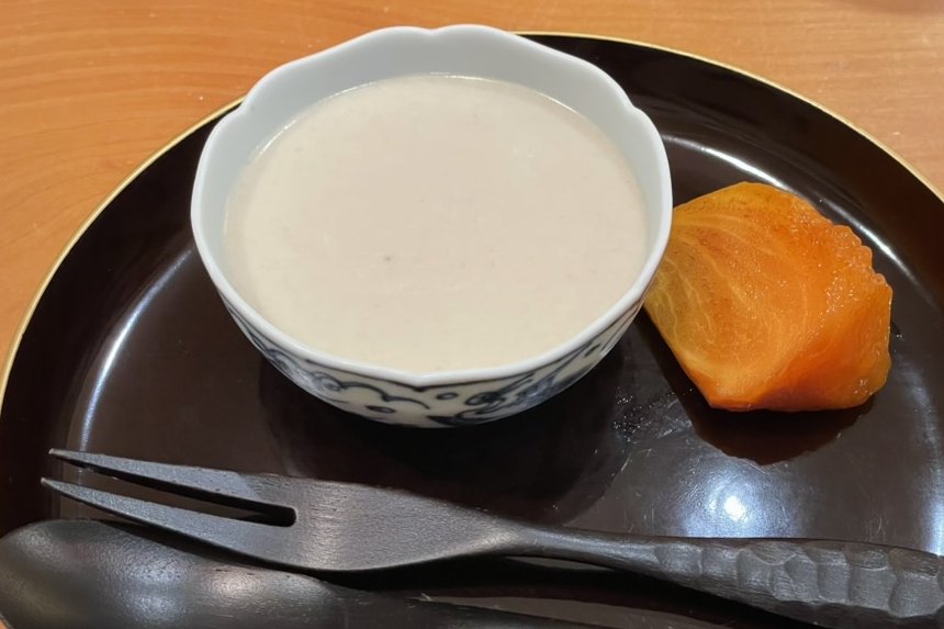 A bowl of cold milky pudding beside a piece of candied persimmon on a black plate