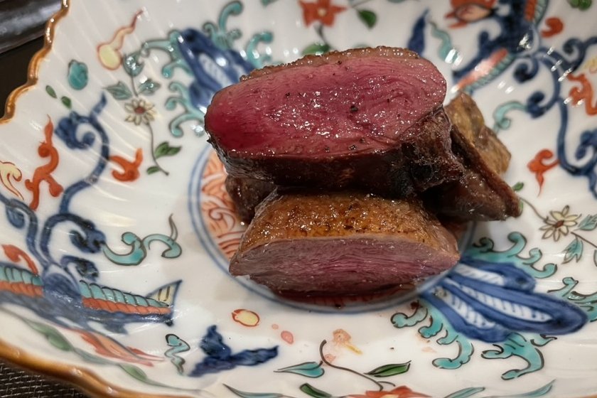 Slices of rare roast duck breast stacked on a colourful kutani plate