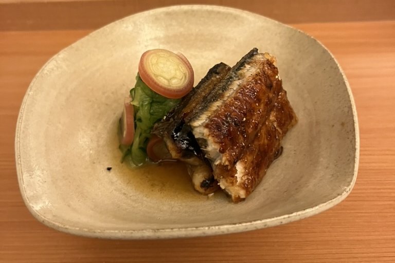 Glazed grilled eel in a ceramic bowl, set over a cool vinegared garnish