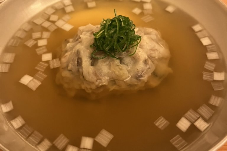 A clear dashi soup with a shinjo dumpling topped with shredded green union