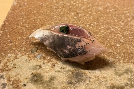 An aji nigiri with grated ginger and scallion on a stone plate