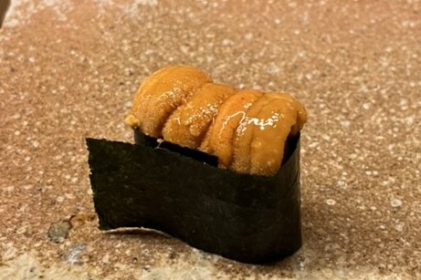 A uni gunkan wrapped in nori on a stone plate