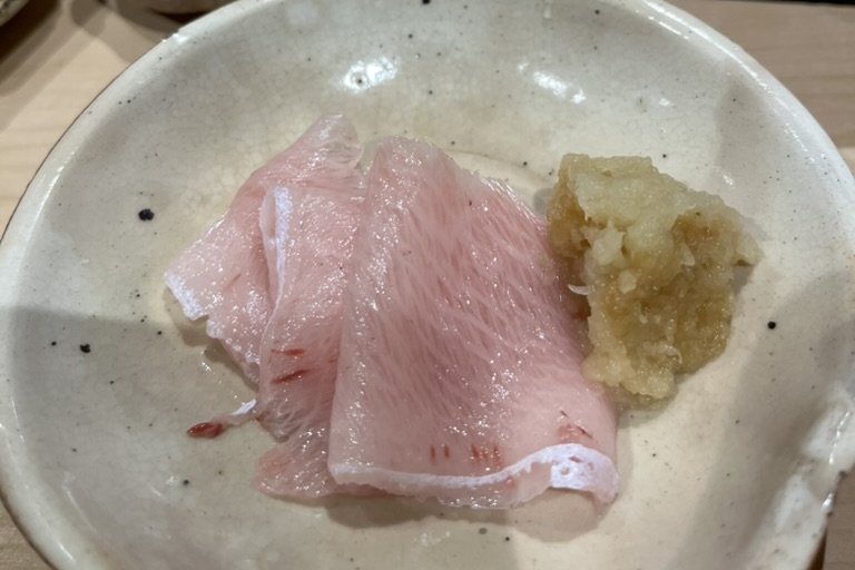 Slices of fatty pink kan-buri (winter yellowtail) sashimi with grated ginger in a ceramic bowl