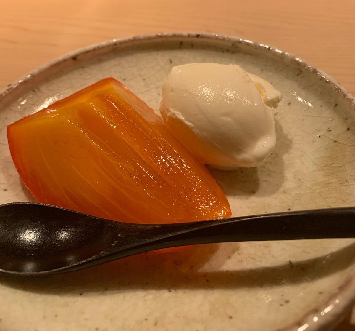 A slice of glossy ripe persimmon with a quenelle of cream on a ceramic plate