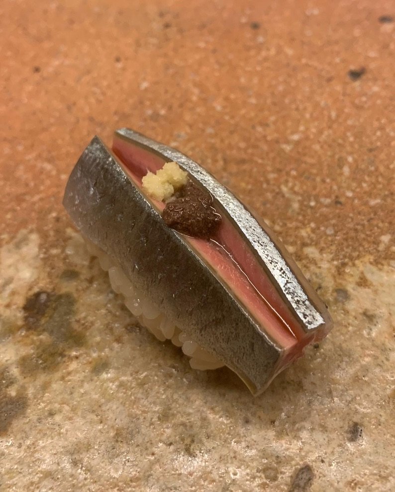 A fatty sanma (Pacific saury) nigiri with silver skin and grated ginger on a stone plate