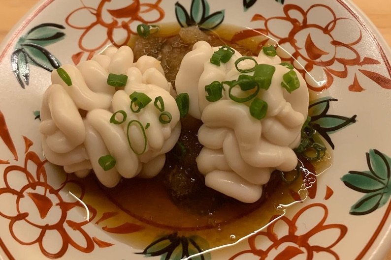 Two creamy lobes of shirako (cod milt) in ponzu with grated daikon and scallion, on a floral plate