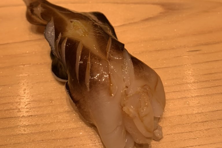A torigai (cockle) nigiri, its dark-edged mantle glossy, on a hinoki counter