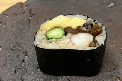 A cut futomaki thick roll showing egg, cucumber, shrimp and kanpyo